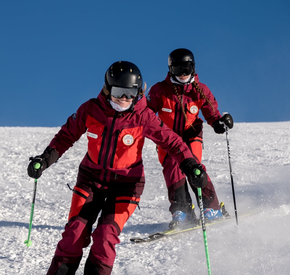 Two Evolution Ski School instructors skiing with poles on a Zermatt piste